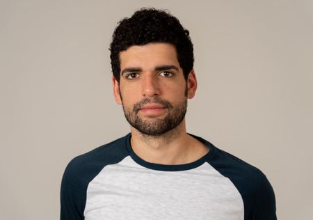 Close up headshot of young latin man with natural and neutral face expression with beard and dark hair. Isolated on neutral background. In People fashion, Lifestyle Beauty and Human emotions.の写真素材
