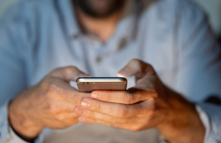 Close up of teenager or adult man playing online and sending text on smart phone with a colorful background light from the screen in Mobile addiction Internet gaming Connections and New technology.の写真素材