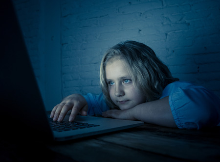 Cute schoolgirl child playing and surfing online late at night. Child addicted to internet games and social media canÂ´t sleep hooked on laptop. Digital technology in childhood and internet addiction.の写真素材