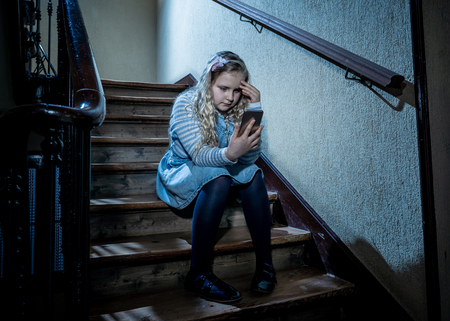 Sad depressed girl Bullied by text message humiliated online social media by classmates. Sad depressed young girl victim of cyberbullying by mobile phone sitting on stairs feeling lonely hopeless.の写真素材
