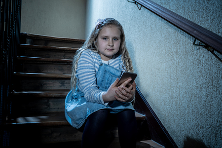 Sad depressed girl Bullied by text message humiliated online social media by classmates. Sad depressed young girl victim of cyberbullying by mobile phone sitting on stairs feeling lonely hopeless.の写真素材