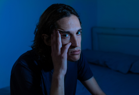 Devastated millennial man crying sad feeling hurt and hopeless suffering Depression. Depressed teenager victim of bullying or abuse sitting on bed alone in despair at night. In teenage Mental health.の写真素材