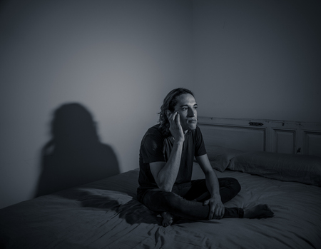 Devastated millennial man crying sad feeling hurt and hopeless suffering Depression. Depressed teenager victim of bullying or abuse sitting on bed alone in despair at night. In teenage Mental health.の写真素材