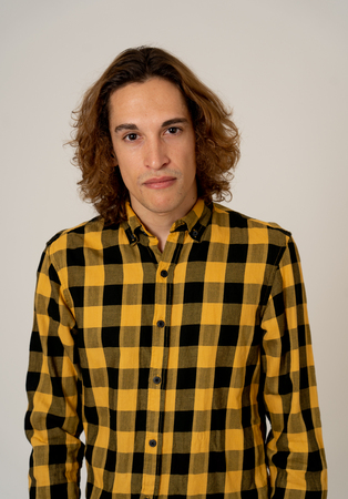 Studio portrait of young teenager man with brown long hair wearing checked shirt feeling confident and relaxed posing and modeling. Isolated on neutral background. In lifestyle and youth culture.の写真素材