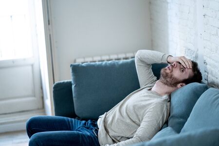 Unhappy depressed caucasian male sitting and lying in living room couch feeling desperate a lonely...