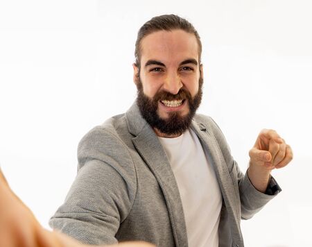 Young funny bearded hipster blogger man in modern casual style holding camera or smart phone shooting self portrait or recording video for his followers. In internet social media, blog concept.の写真素材