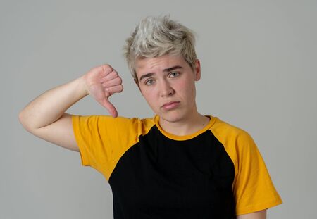 Portrait of young good looking teenager boy making thumbs down feeling disappointed and unhappy. Studio shot isolated on neutral background in people and Human emotions and expressions concept.の写真素材