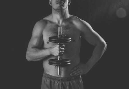 Portrait of young muscular built athlete man working out doing exercises and posing with dumbbells, bodybuilder male naked torso lifting weights in Fitness sports Body care and healthy lifestyle.の写真素材