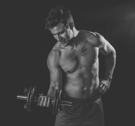 Portrait of young muscular built athlete man working out doing exercises and posing with dumbbells, bodybuilder male naked torso lifting weights in Fitness sports Body care and healthy lifestyle.の写真素材
