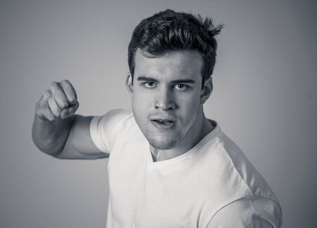 Young attractive man in rage looking furious in defence stance and threaten punching with fist in angry upset and mad face expression isolated grey background in youth violence and aggression concept.の写真素材