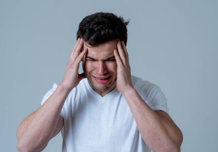 Close up of young sad latin man with strong headache and migraines looking worried in emotional pain. Feeling sorrow and depression. Isolated in neutral background in People and Health care concept.の写真素材