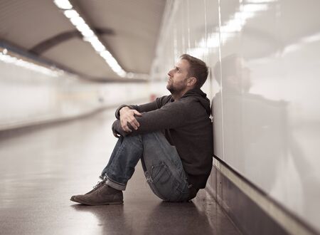 Sad young man crying suffering depression stress sitting on ground street subway tunnel looking desperate leaning on wall alone in Mental disorder Emotional pain Addiction and Unemployment concept.の写真素材