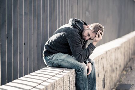 Young attractive man suffering from depression stress sitting alone and sad on the street feeling anxious and lonely in unemployment Mental health Drug and alcohol addiction concept.の写真素材