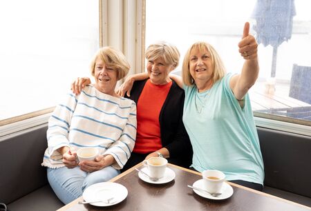 Joyful elderly friends having tea or coffee together. Senior girlfriends chatting laughing and...