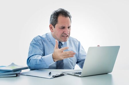 Angry and frustrated middle aged businessman overworked at desk upset with laptop in adults perception and use of technology, Overtime, stress at work concept isolated in white background.の写真素材