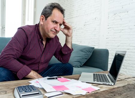 Mature attractive man on computer looking stressed and worried with credit card payments and home finances accounting costs charges taxes and mortgage in paying bills financial problems and debts.の写真素材