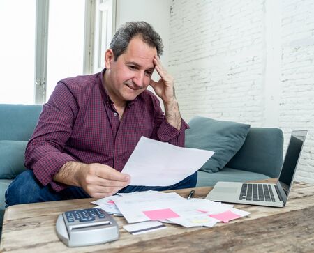 Mature attractive man on computer looking stressed and worried with credit card payments and home finances accounting costs charges taxes and mortgage in paying bills financial problems and debts.の写真素材