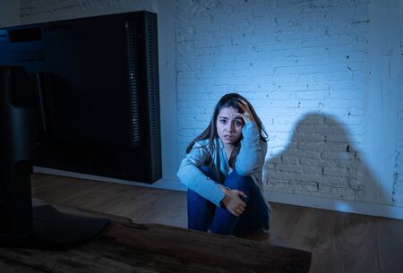 Dramatic portrait of intimidated depressed young woman on ground staring at computer suffering harassment and cyberbullying. Being online abused by stalker feeling desperate. Dangers of in Internet.の写真素材