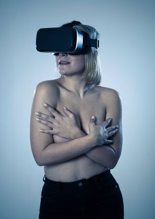 Sensual attractive woman using augmented or virtual reality goggles feeling excited exploring virtual sexuality while getting topless covering her breast. In cyber sex VR simulator and new technology.の写真素材