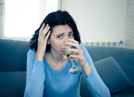 Portrait of depressed woman drinking glass of wine alone at home. Feeling distress, hopeless and...