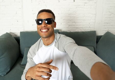 Young attractive african american blogger man in modern casual style holding camera or smart phone...