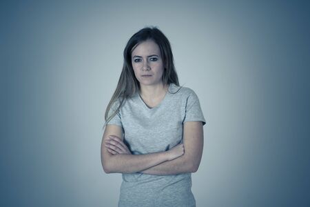 Portrait of Young pretty caucasian teenager with angry face looking worried and disgusted with arms crossed . Studio shot with moody light. Facial expressions and emotions or adolescent mental health.の写真素材
