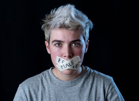 Transgender teenager with mouth sealed on tape with words male and female written in social taboo of gender diversity concept. Trans boy not able to communicate or be free to express his own identity.の写真素材