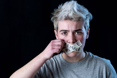 Transgender teenager with mouth sealed on tape about to break his silence about own gender identity in Breaking social taboos and freedom concept. Human rights Equality and Gender Diversity campaign.の写真素材