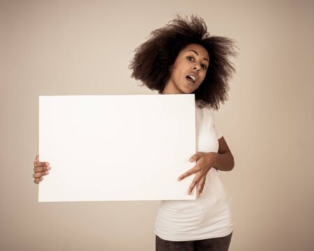 Funny and beautiful african american woman showing and pointing at blank board with copy space for...