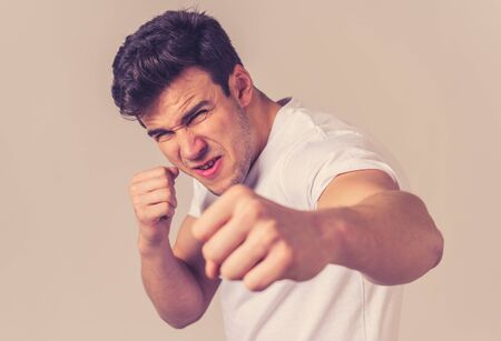 Young attractive man in rage looking furious in defence stance and threaten punching with fist in angry upset and mad face expression isolated grey background in youth violence and aggression concept.の写真素材