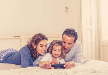 COVID-19 Quarantine. Stay home Stay connected. Happy Mom dad and little daughter girl with mobile phone on video call talking to family and friends during coronavirus self isolation and lockdown.の写真素材