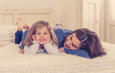 COVID-19 Lockdown. Happy family Mother and cute daughter hugging, playing and laughing together in bed in quarantine during coronavirus Outbreak. Stay home save lives, stop the virus spread concept.の写真素材