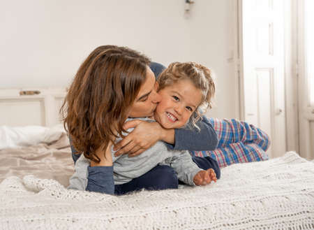 COVID-19 Lockdown. Happy family Mother and cute daughter hugging, playing and laughing together in bed in quarantine during coronavirus Outbreak. Stay home save lives, stop the virus spread concept.の写真素材