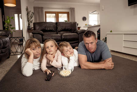 Coronavirus lockdow. Bored family watching tv helpless in isolation at home during quarantine COVID 19 Outbreak. Mandatory lockdowns and self isolation recommendations forces families stay home.の写真素材