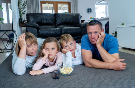 Coronavirus lockdow. Bored family watching tv helpless in isolation at home during quarantine COVID 19 Outbreak. Mandatory lockdowns and self isolation recommendations forces families stay home.の写真素材