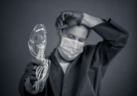 COVID-19 Outbreak. Exhausted Doctor holding non- invasive ventilator. Medical treatment and lack of equipment for coronavirus infected patients with SARS. Shortage of medical ventilators in hospitals.の写真素材