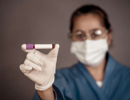 COVID-19. Doctor or lab technician scientist in PPE Personal Protective Equipment holding blood sample tube of infected patient at hospital. Coronavirus blood test for antibodies and vaccine research.の写真素材