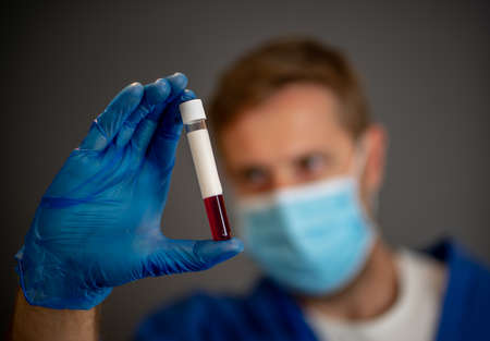 COVID-19. Doctor or lab technician scientist in PPE Personal Protective Equipment holding blood sample tube of infected patient at hospital. Coronavirus blood test for antibodies and vaccine research.の写真素材