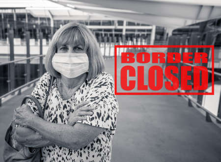 COVID-19 Outbreak impact. Traveler woman with face mask at airport affected by flight cancellation for coronavirus pandemic and worldwide countries shutdowns. Border closed written in red.の写真素材