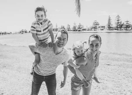 Happy family portrait of mother, father, son and daughter having fun together in the park. Boy and little girl enjoying time with their parents. Positive emotion, parenting and childhood concept.の写真素材