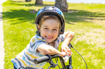 Cute cheerful boy with helmet on his new bike by the lake at the park. Lifestyle portrait of happy kid on his bicycle. Outdoor activities, vacations, happy childhood and back to normal concept.の写真素材