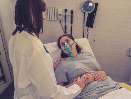 Female doctor with young sick woman patient with Oxygen Mask looking in pain and worried in...