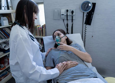 Female doctor with young sick woman patient with Oxygen Mask looking in pain and worried in...