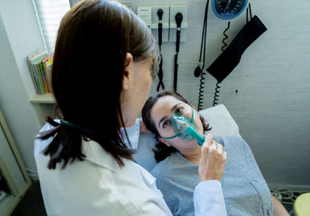 Female doctor with young sick woman patient with Oxygen Mask looking in pain and worried in...
