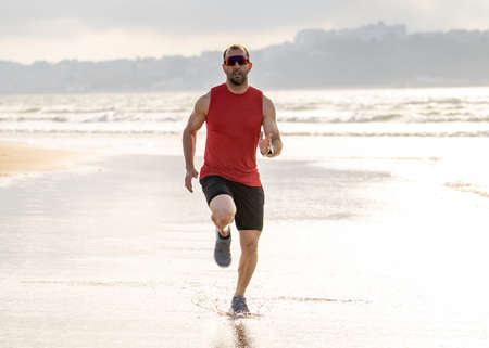 Athlete runner man running, sprinting and training in sport wear on beach at sunset. Fitness model...