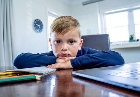 Coronavirus Outbreak. Lockdown and school closures. School boy with face mask watching online education classes feeling bored and depressed at home. COVID-19 pandemic forces children online learning.の写真素材