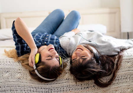 COVID-19 lockdown. Confident and optimistic women best girlfriends laughing listening online music singing and dancing together in bed at home in isolation. Stay home safe health and safety campaign.の写真素材