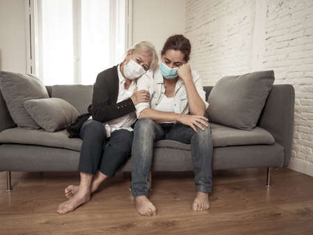 Depressed senior mother and daughter wearing medical mask crying and embracing each other grieving...