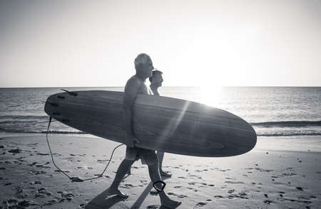 Two mature men walking with surfboards on beautiful beach enjoying paradise and retirement...