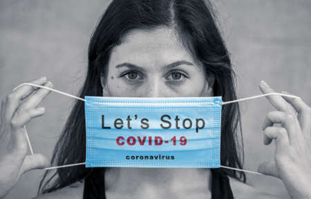 Strong image of Young woman wearing medical protective surgical face mask with text Stop The Coronavirus Spread. Conceptual portrait of Protection against Covid-19 coronavirus outbreak campaign.の写真素材